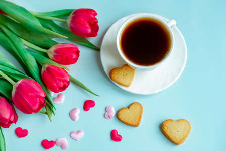 a cup of coffee in a white cup, with scattered hearts and red tulips on a blue background.の写真素材