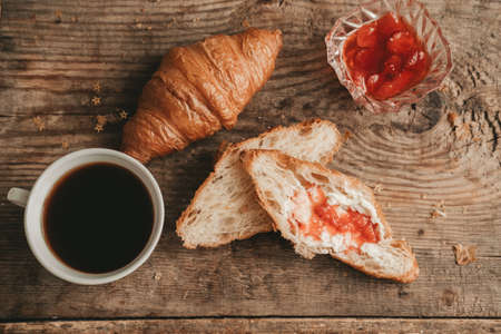 cut croissant with butter and strawberry jam with a cup of coffee, on a wooden background, top view.の写真素材