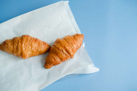 2 large croissants on white paper, on a blue background. Morning breakfast in France.