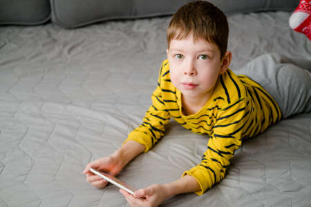 a teenage boy lies on the couch with a phone in his hands. The child plays at home in the phone....