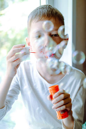 Boy blowing soap bubbles sitting on sofa at home. a lot of soap bubbles. Interesting games at home....