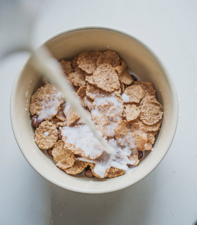 pouring milk into a white bowl with corn flakes, top view