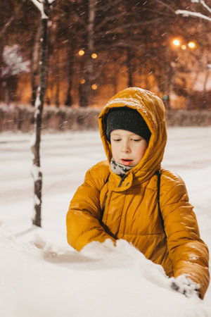 a boy in a yellow jacket plays with snow during a snowfallの写真素材