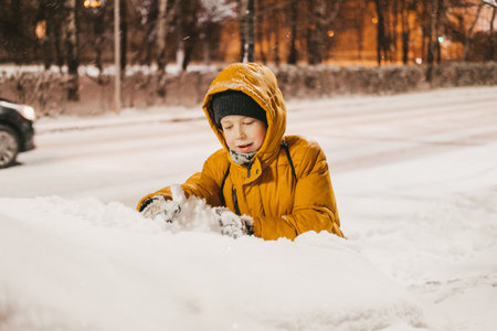 a boy in a yellow jacket plays with snow during a snowfallの写真素材