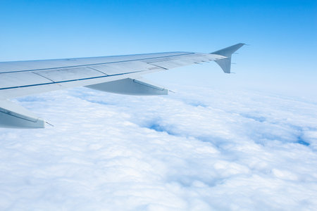 Wing of an airplane flying over white clouds and blue skyの写真素材