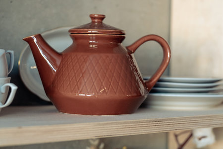 brown clay teapot on a white shelf with cups and platesの写真素材