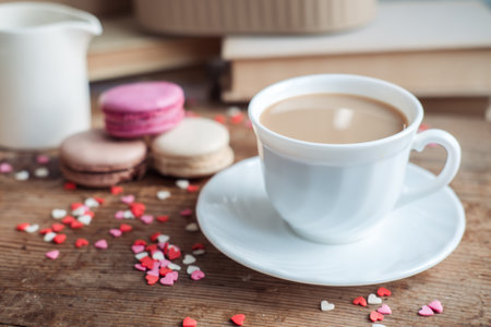 Macaroons and a cup of coffee, a milk jug on a background of small hearts on a wooden background, top viewの写真素材