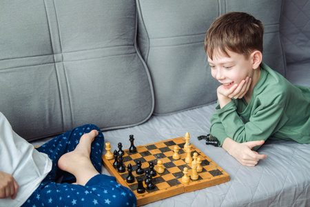 Boys play wooden chess lying on a gray sofa.の写真素材