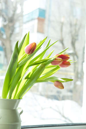 a bouquet of tulips in an iron vase on the windowsill, against the backdrop of a snowy cityの写真素材