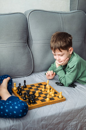Boys play wooden chess lying on a gray sofa.の写真素材
