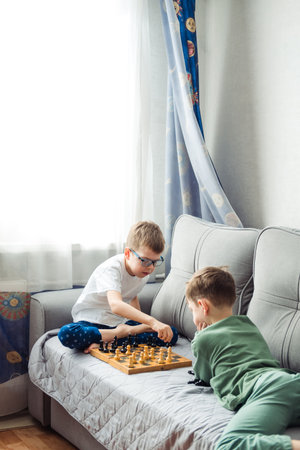 Boys playing wooden chess lying on a gray sofa in front of the windowの写真素材