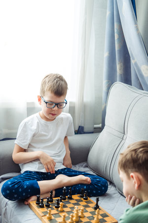 Boys playing wooden chess lying on a gray sofa in front of the windowの写真素材