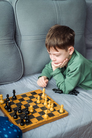 Boys play wooden chess lying on a gray sofa.の写真素材
