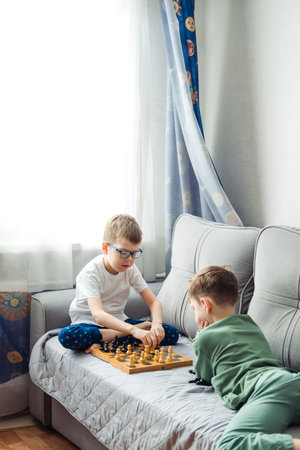 Boys playing wooden chess lying on a gray sofa in front of the windowの写真素材