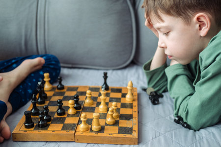 Boys play wooden chess lying on a gray sofa.の写真素材