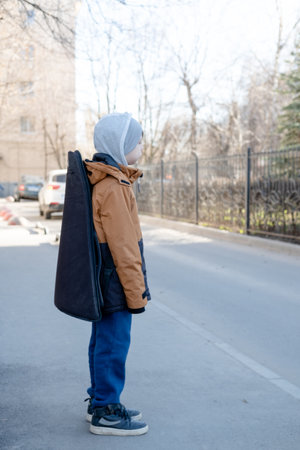 A teenage boy in a jacket and hat walks alone with a guitar in a case. Child musician lost in the cityの写真素材