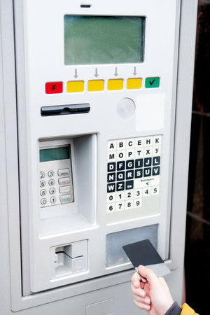 The hand holds the card and approaches the parking payment terminal for paymentの写真素材