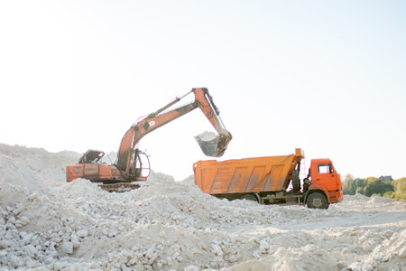 The excavator collects stones in a bucket and puts them in a truck. Working machines at road constructionの写真素材