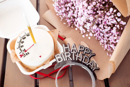 Bento cake with a candle with a bouquet of pink gypsophila on a wooden table, in a cafe. Little surprise for a girl's birthdayの写真素材