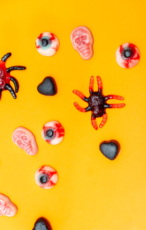 Halloween jelly candies in skulls, vampire teeth, black hearts, bones, spiders, on an orange background with a hard shadow. Festive pattern of sweets, treats.の写真素材