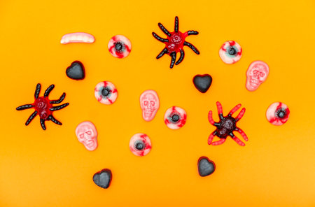 Halloween jelly candies in skulls, vampire teeth, black hearts, bones, spiders, on an orange background with a hard shadow. Festive pattern of sweets, treats.の写真素材