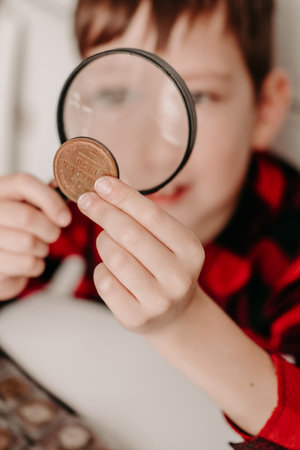 collecting coins The boy examines an old coin through a magnifying glass. Dollars, euros on the table. Money of different nations. Savings in the form of currencies and coinsの写真素材