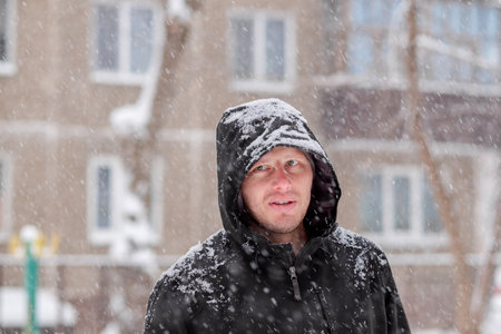 man in a hood during a snowfall. Portrait of a man in winter. Serious lookの写真素材