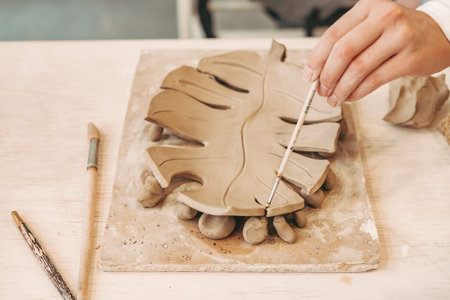 Clay craft. Handmade. Clay plate in the shape of a Monster. Girl working with a brush in the workshopの写真素材