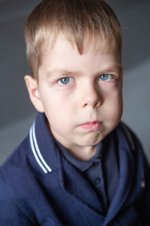 portrait of a 6 year old boy with blond hair and blue eyes indoors, with a serious expression on his faceの写真素材