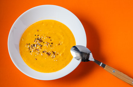 pumpkin cream soup with sesame seeds on a bright background. Yellow soup on an orange background.の写真素材