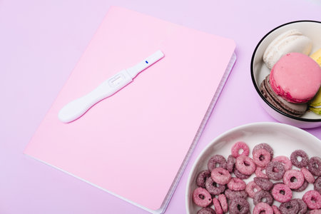 pregnancy test on a pink notebook, against the background of a purple table. Planning a pregnancy for a student. Sweet breakfast with cereal for a pregnant womanの写真素材