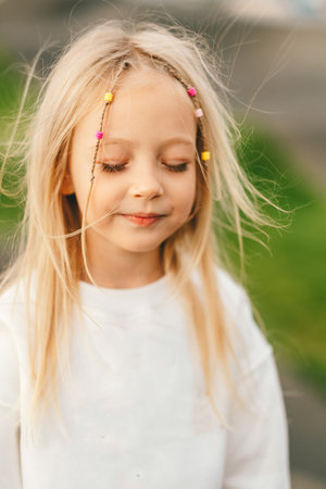 Portrait of a smiling little blonde girl with her hair flowing in the wind. Blonde hair with baubles in the windの写真素材
