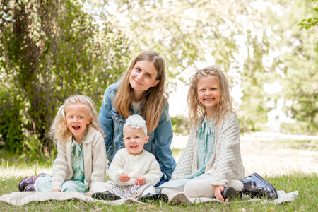 mother with three daughters sits on a picnic in the summer and looks into the frame. mother with three blonde daughters walks in the park. Mother of many children daughtersの写真素材