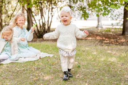happy little girl in white tights and headbands on a picnic with her sisters. The baby is learning to walk.の写真素材