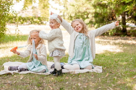 3 sisters at a picnic playing with soap bubbles. Summer holidays 3 blonde girls. large familyの写真素材