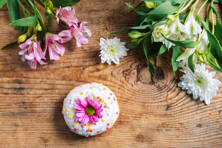 chamomile bud on top of a donut on a wooden background with a bouquet of alstroemerias and chrysanthemums. Delicate frame with pink flowerの写真素材