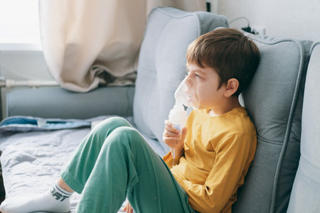 little boy sits with an inhalation mask during cough and bronchitis. Treatment with an inhaler at homeの写真素材