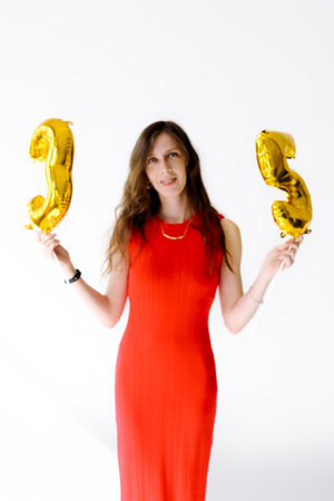 Beautiful woman with balloons and the numbers 35 is photographed in the studio in a red dress....