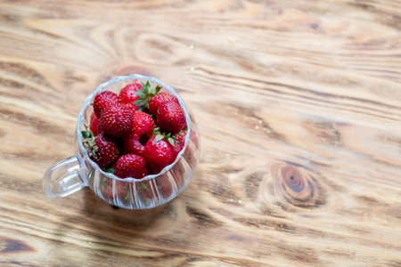 Strawberry harvest in a transparent cup on a wooden background, top viewの写真素材