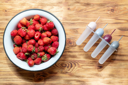 strawberry harvest in an iron bowl on a wooden background, top viewの写真素材