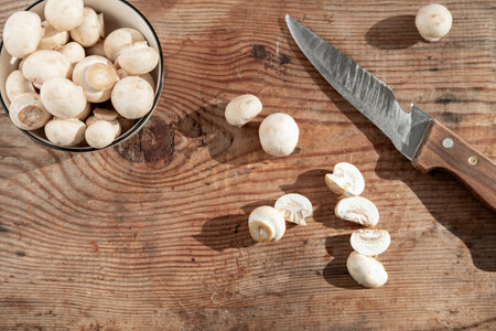 large knife and fresh, small champignons close-up in a bowl, on a wooden background