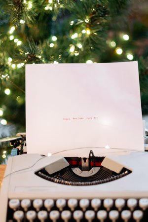 On the paper, typewritten: Happy New Year 2025, against the background of a Christmas tree with garlandの写真素材