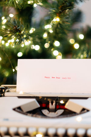 On the paper, typewritten: Happy New Year 2025, against the background of a Christmas tree with garlandの写真素材
