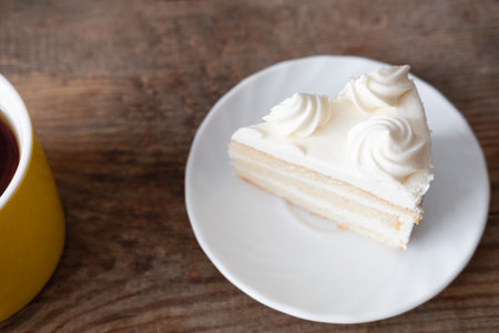 black tea in yellow cup and piece of cake with cream on wooden background, top viewの写真素材
