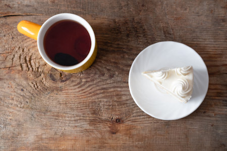 black tea in yellow cup and piece of cake with cream on wooden background, top viewの写真素材