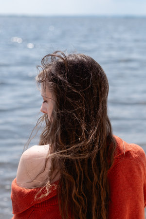 Young woman with long hair dressed in a terracotta sweater, standing with her back to the sea. Sad and romantic moodの写真素材