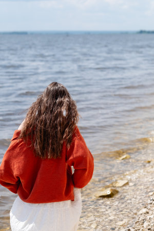 Young woman with long hair dressed in a terracotta sweater, standing with her back to the sea. Sad and romantic moodの写真素材