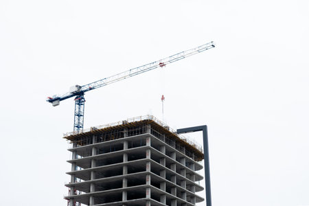 A high-rise crane over an unfinished concrete high-rise building, close-upの写真素材