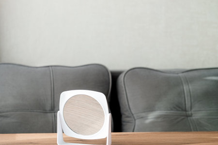 A white round plastic makeup mirror stands on a wooden table against the background of a sofaの写真素材