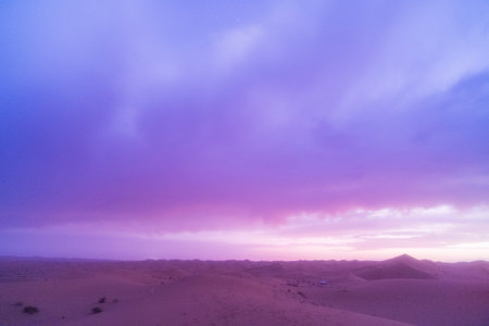 Vast desert sand dunes under a dramatic purple twilight sky with scattered stars and soft clouds.